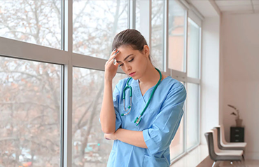 Sad woman in blue shirt looking out window, grieving loss symbolizing wrongful Death